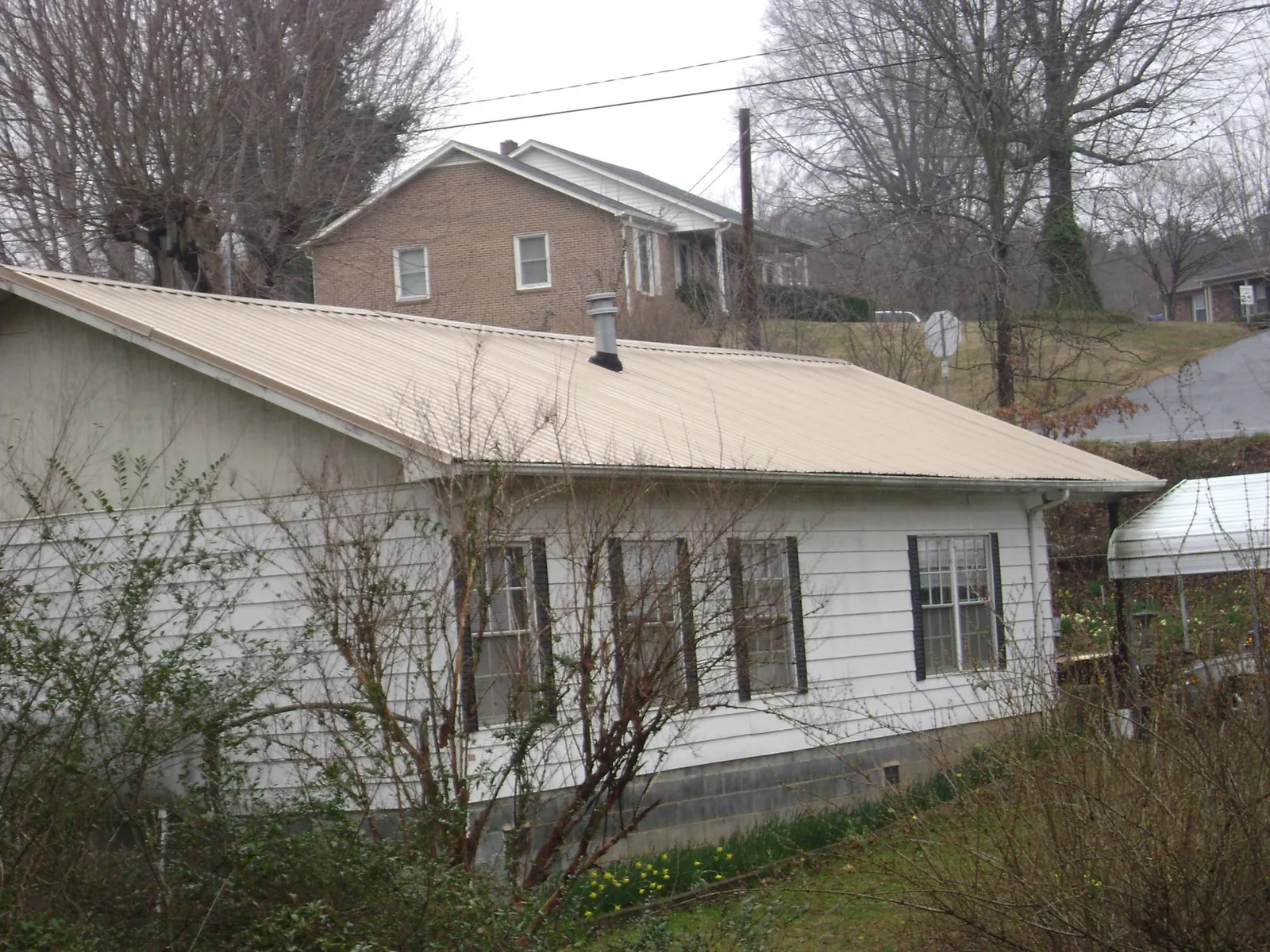 Tan metal roof on a white sided house set into a hillside — Commercial Roofing by Roofing Brothers in Greenbackville